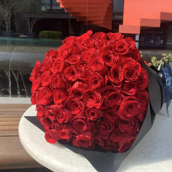 Large bouquet of tightly packed red roses wrapped in black paper with a blue ribbon