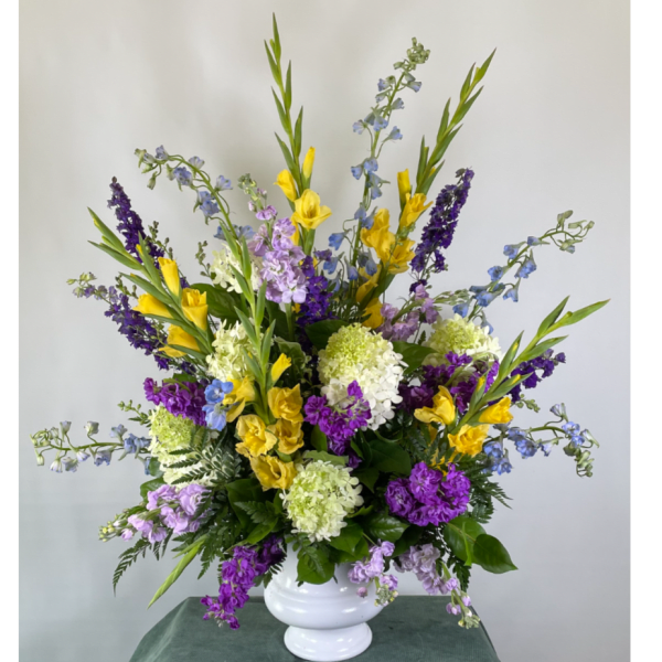 Tall mixed bouquet in a white vase with yellow, purple, blue, and white flowers