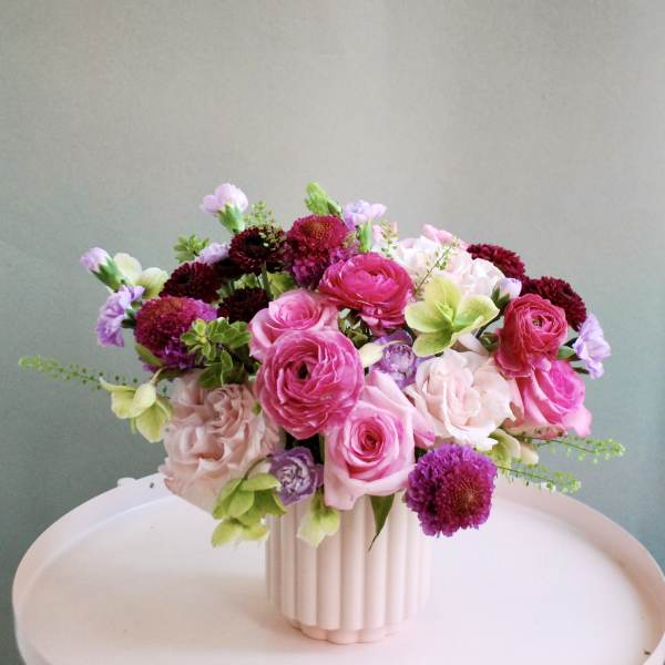 Pink and purple flower arrangement in a ribbed white vase
