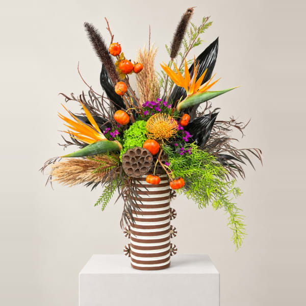 Tropical arrangement with orange bird-of-paradise in a striped vase