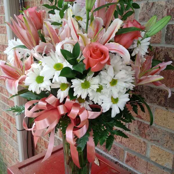 Pink roses and lilies with white daisies in a clear glass vase