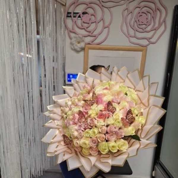 Large bouquet of pastel roses with butterfly accents and layered wrapping