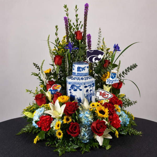 Large floral arrangement with red roses, lilies, and blue hydrangeas around a blue-and-white vase