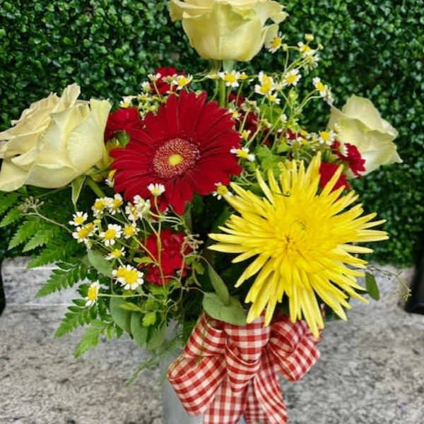 Mixed bouquet with red, yellow, and white flowers in a metal vase with a gingham ribbon