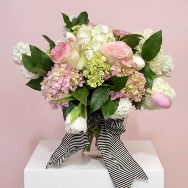 Pink and white roses, hydrangeas, and tulips in a glass vase with a striped ribbon