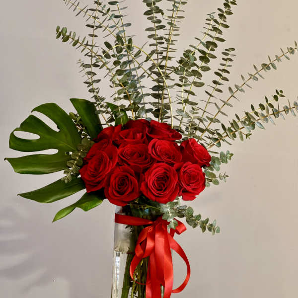 Red roses in a tall glass vase with eucalyptus and a red ribbon