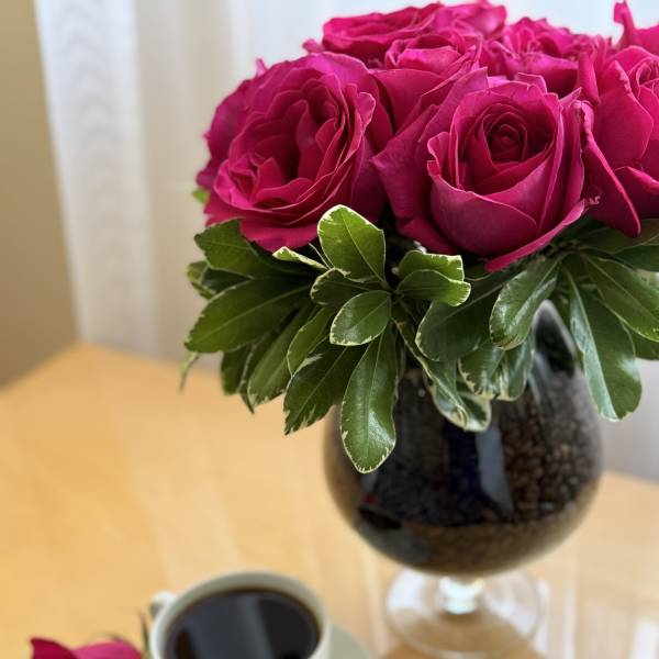 Pink roses in a glass vase beside a cup of coffee
