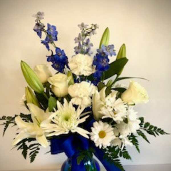 White and blue floral arrangement in a glass vase with a blue ribbon