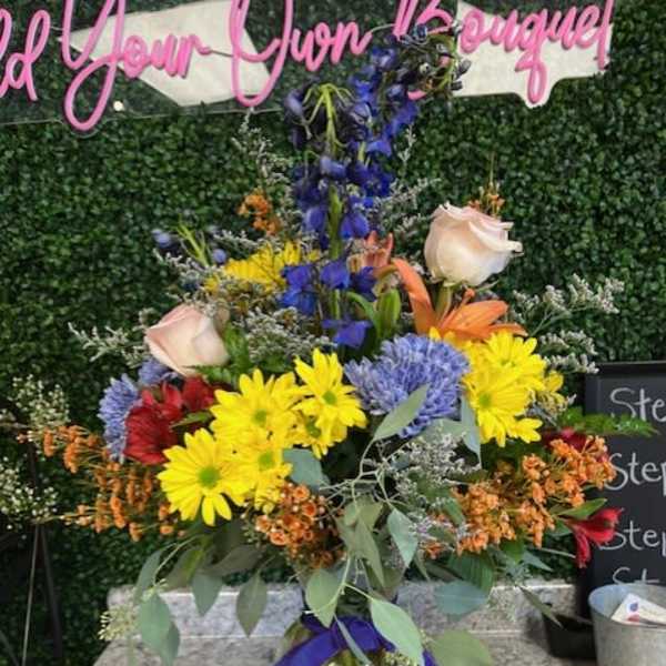 Colorful mixed flower arrangement in a glass vase with a purple ribbon