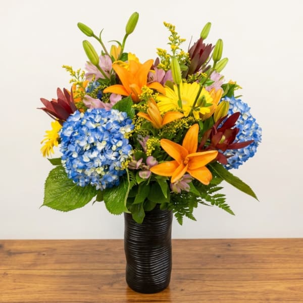 Colorful bouquet of lilies, hydrangeas, and daisies in a black vase