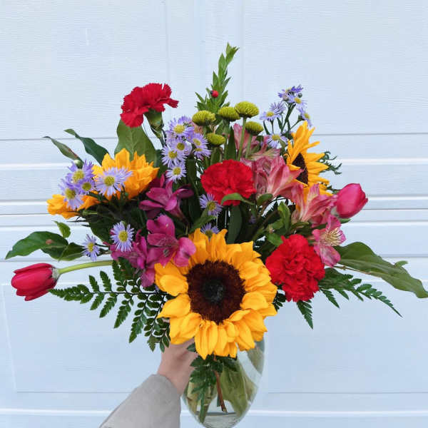Mixed bouquet with sunflowers, red carnations, and pink tulips in a glass vase