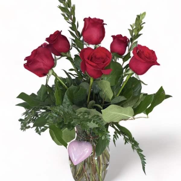 Red roses in a clear glass vase with a pink heart decoration