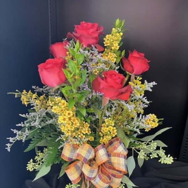 Red roses in a glass vase with yellow filler flowers and a plaid bow