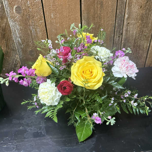 Low mixed arrangement with yellow roses, white and pink carnations, and small pink blooms.