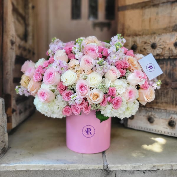 Large arrangement of pink, white, and peach roses in a round pink hatbox-style container.