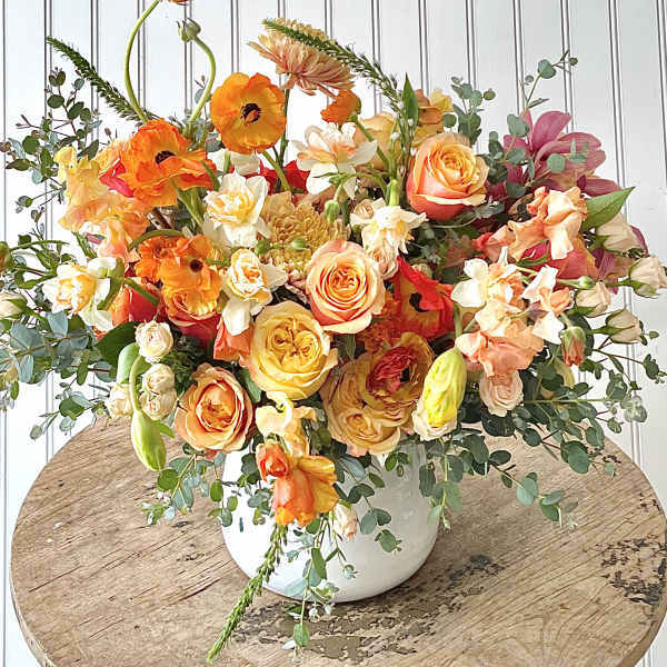 Colorful bouquet of orange, peach, and white flowers in a white vase