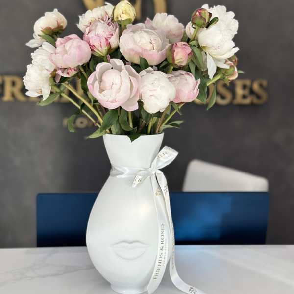 Pink and white peonies in a white face vase with ribbon