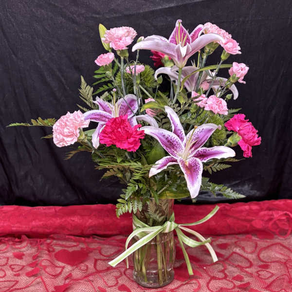Pink carnations and lilies arranged in a glass vase with a ribbon.