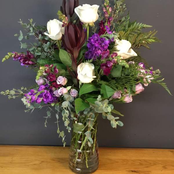 Bouquet of white roses and purple flowers in a glass vase
