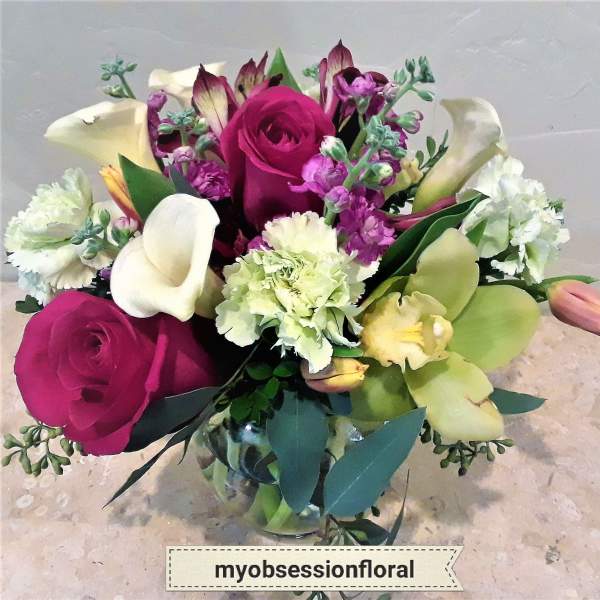 Bouquet of magenta roses, white calla lilies, and purple flowers in a glass vase