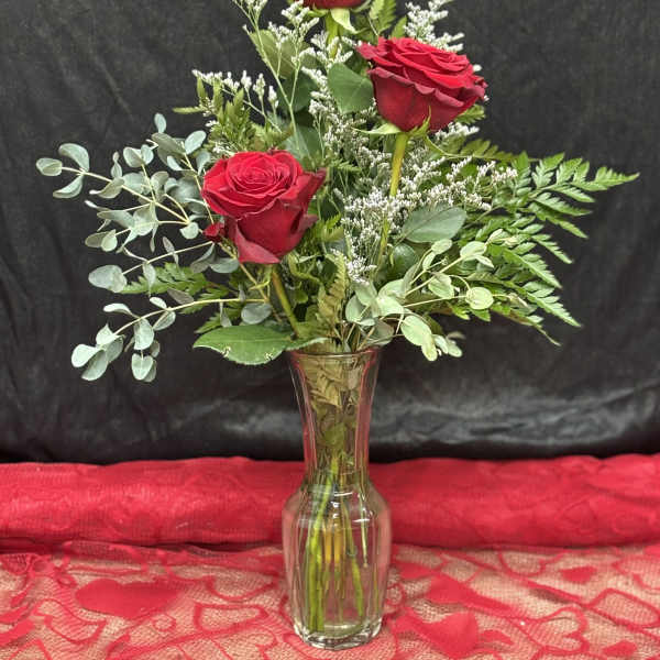 Three red roses in a clear glass vase with mixed greenery