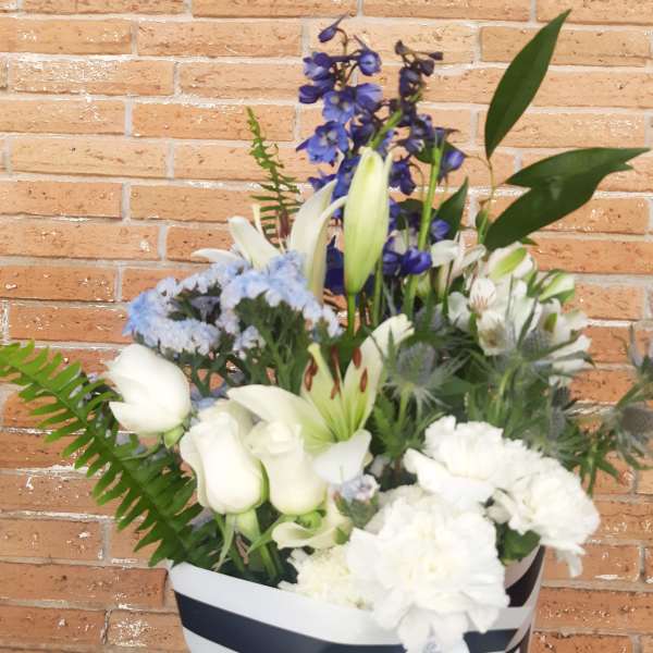 White lilies and carnations in a striped gift box with blue flowers