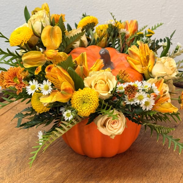 Fall floral arrangement in a pumpkin container with yellow and orange blooms