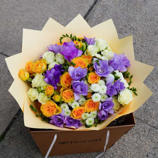 Bouquet of purple, orange, yellow, and white roses in cream wrapping
