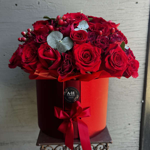 Red roses arranged in a round red hat box with a ribbon
