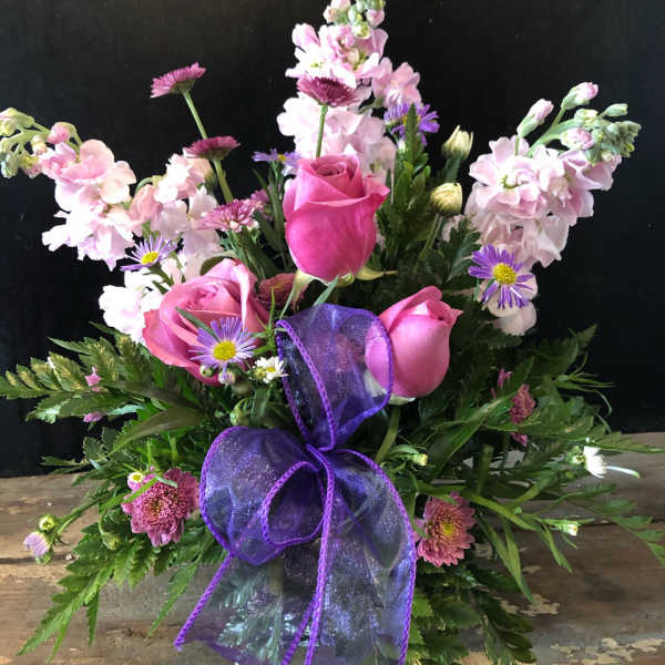 Pink roses and purple flowers arranged with a purple ribbon