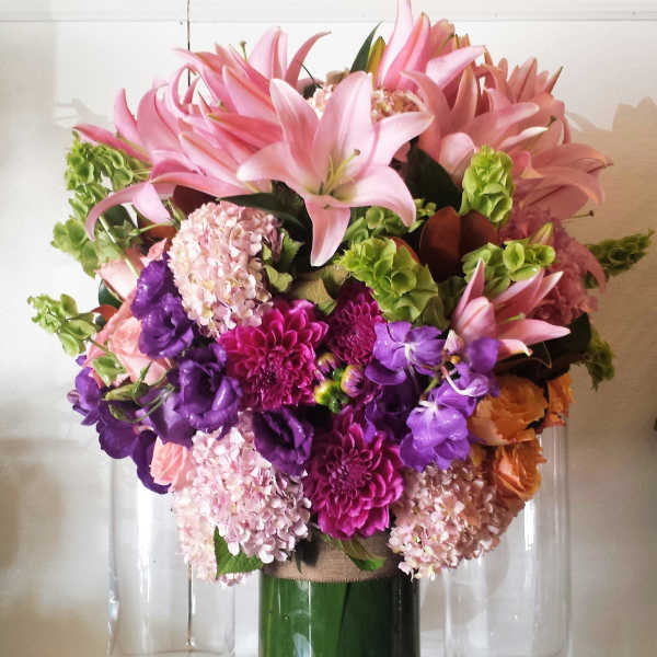Pink lilies and purple flowers arranged in a tall glass vase