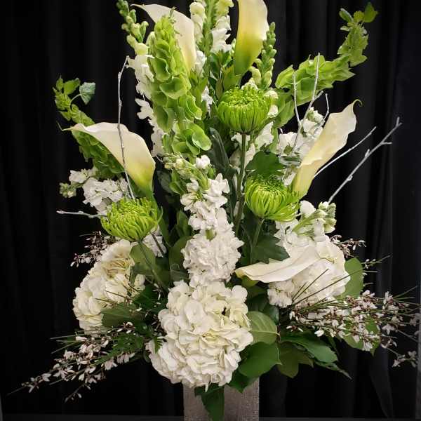 Tall white floral arrangement with calla lilies and green blooms in a square vase