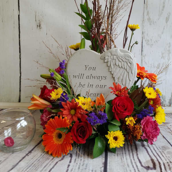 Heart-shaped memorial plaque surrounded by colorful flowers and a glass candle holder