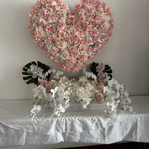 Heart-shaped pink rose arrangement above white orchids and pale flowers