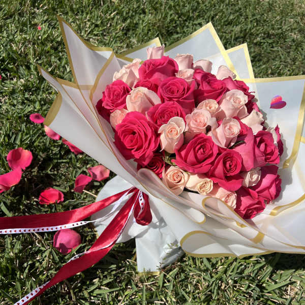 Bouquet of pink and blush roses wrapped in white paper with gold trim