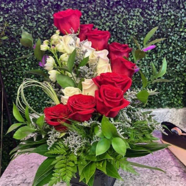 Red and white roses arranged in a black vase with greenery