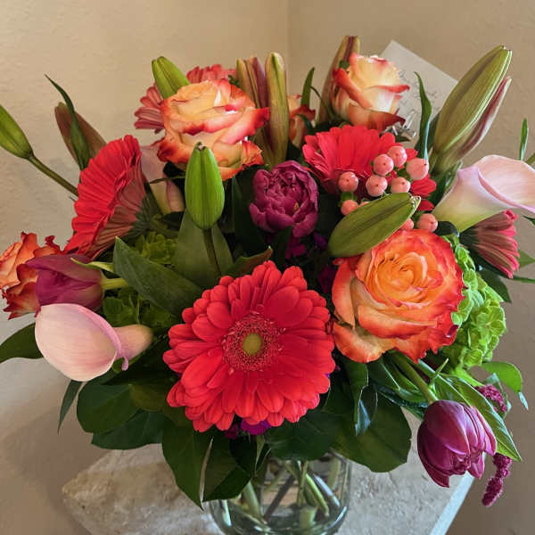 Mixed bouquet of pink, coral, and red flowers in a glass vase