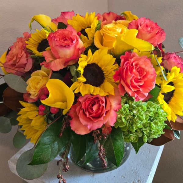 Bouquet of pink roses, yellow sunflowers, and yellow calla lilies in a glass vase