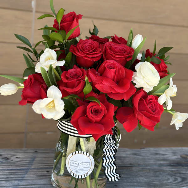Red roses and white flowers arranged in a glass vase with a striped ribbon.
