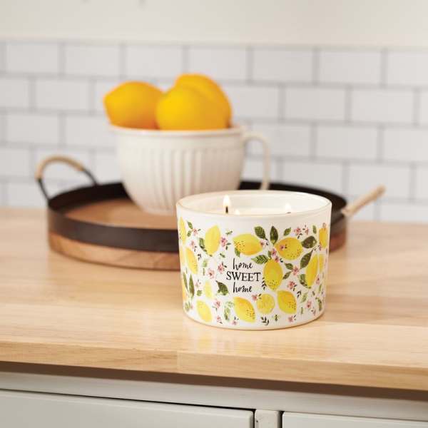 Lemon-patterned candle on a wooden counter with a bowl of lemons behind it