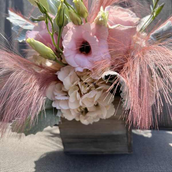 Pink and white floral arrangement with feathery pink accents in a wooden container