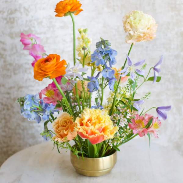 Colorful mixed flower arrangement in a low gold bowl vase on a light table