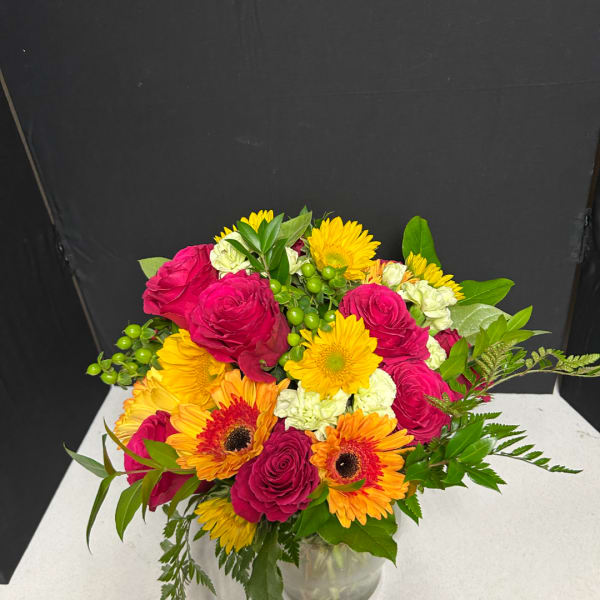 Mixed bouquet of pink roses and yellow-orange gerbera daisies in a glass vase