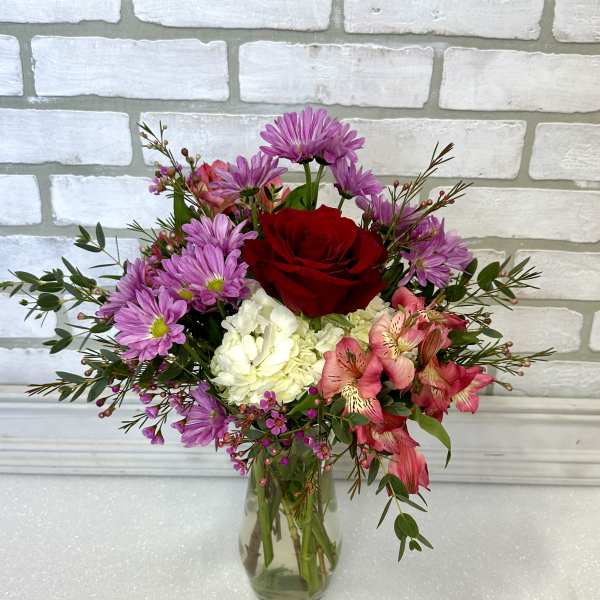 Mixed bouquet of red, pink, purple, and white flowers in a clear glass vase