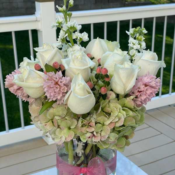 White roses and pink flowers arranged in a glass vase with a pink ribbon