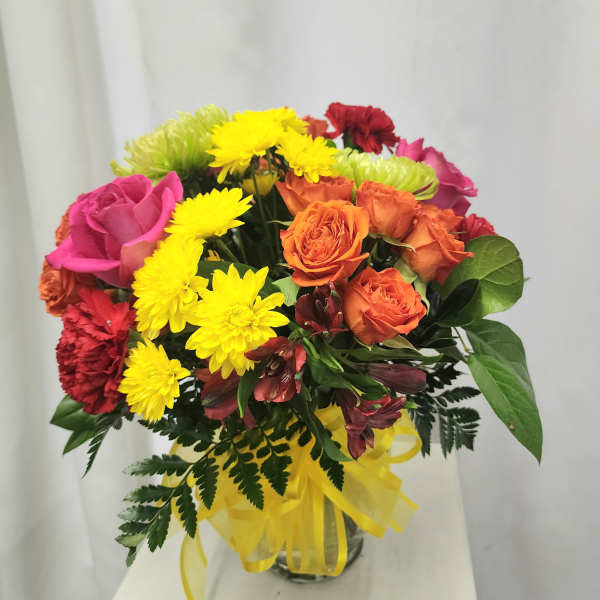 Mixed bouquet of roses and yellow chrysanthemums in a glass vase with a yellow ribbon