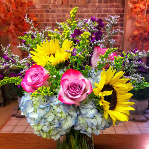 Bright bouquet with pink roses, sunflowers, and blue hydrangeas
