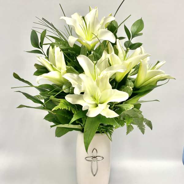 White lilies arranged in a white vase with green foliage