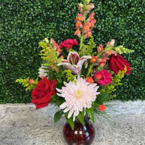 Mixed bouquet with red roses, a white daisy, and lilies in a glass vase