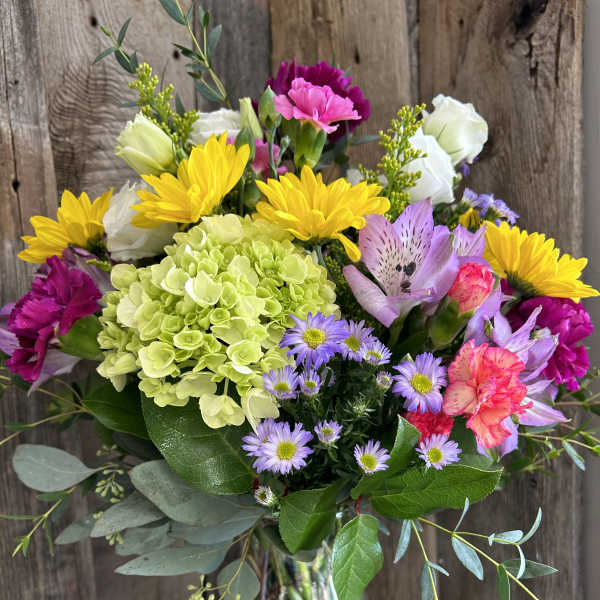 Mixed bouquet of yellow sunflowers, green hydrangea, pink carnations and asters in a clear glass vase